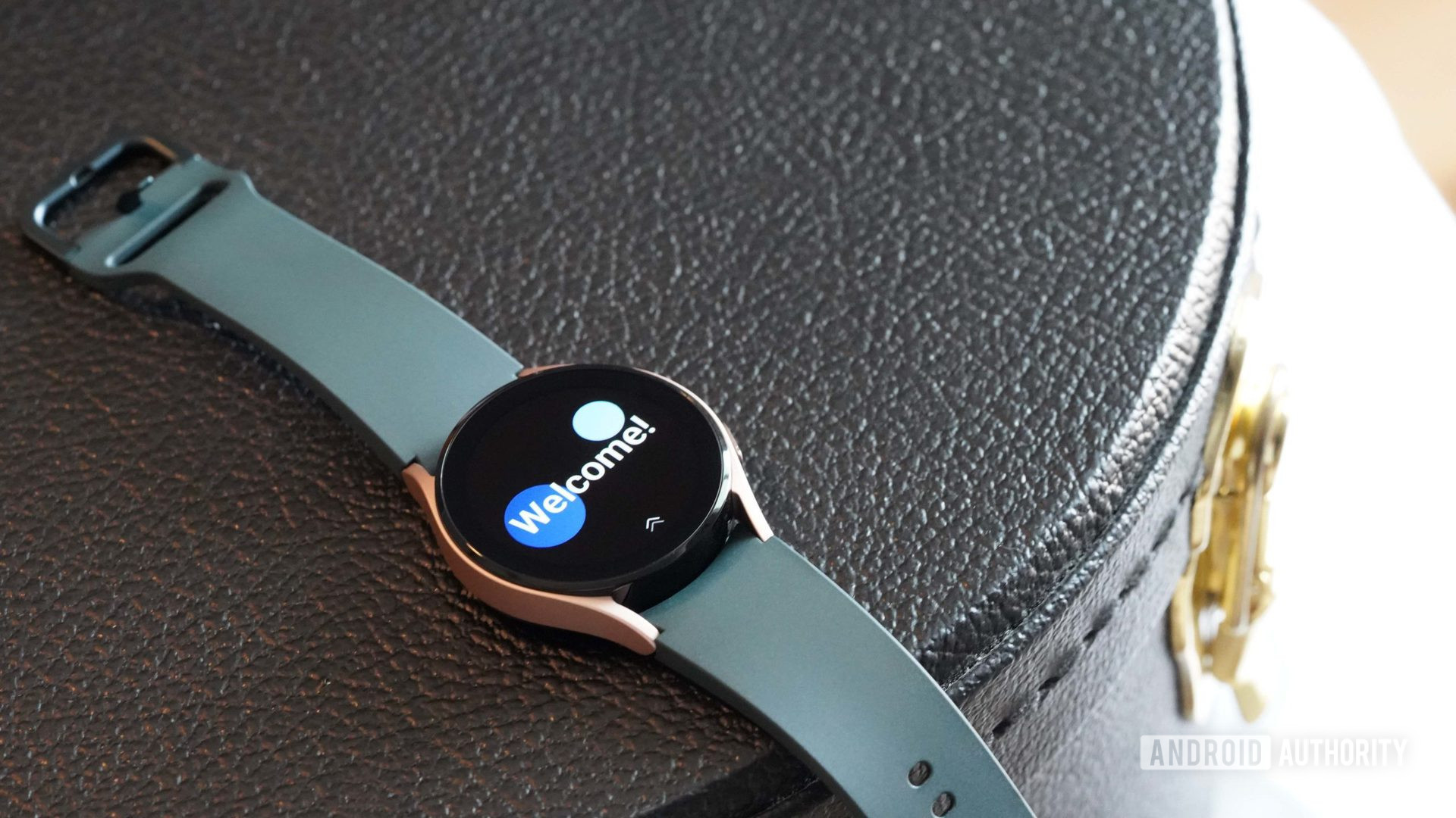 A Samsung Galaxy Watch 4 rests on a black leather case with the watches splash screen.